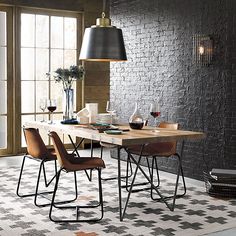 a dining room table with chairs and plants on it in front of a brick wall