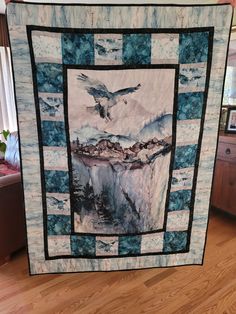 a bird flying over a lake with mountains in the background on a blue and white quilt