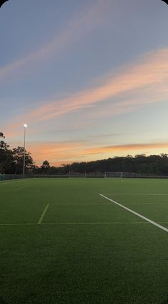 an empty soccer field with the sun setting in the background