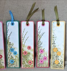 four tags with flowers painted on them hanging from the side of a wall in front of a gray background