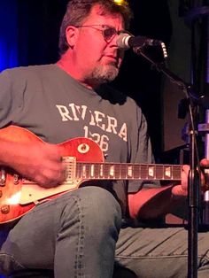 a man sitting in front of a microphone playing a guitar