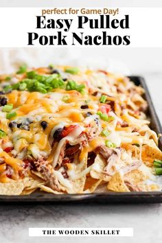 pulled pork nachos on a baking sheet with green onions, cheese and black olives