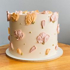 a white cake with pink flowers on it sitting on top of a wooden table next to a wall