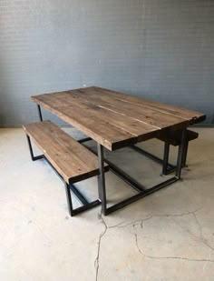 a wooden table with two benches in front of a gray brick wall and concrete floor