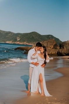 a man and woman standing on top of a beach next to the ocean holding each other