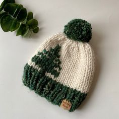 a green and white knitted hat next to a leafy plant on a table