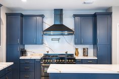 a kitchen with blue cabinets and marble counter tops, an oven hood over the range