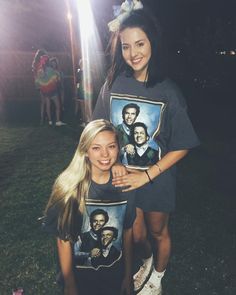 two young women standing next to each other on top of a lush green field at night