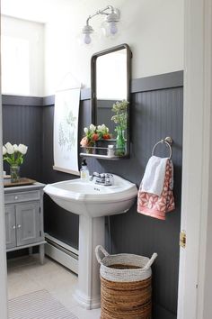 a white sink sitting under a bathroom mirror next to a wooden cabinet with flowers in it