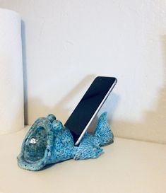 a cell phone sitting on top of a blue ceramic fish next to a roll of toilet paper