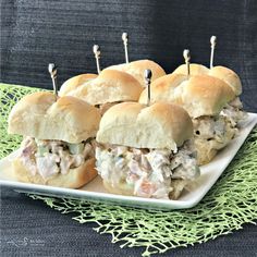 small sandwiches with toothpicks in them sitting on a white plate next to a green tablecloth