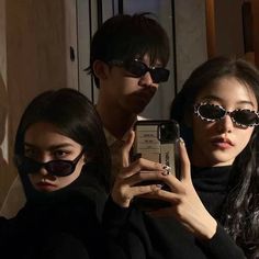 three people wearing sunglasses taking a selfie with their cell phone in front of them