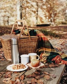 the picnic basket is next to two coffee mugs and a plate with food on it