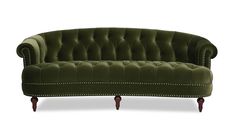 a green velvet couch with wooden legs and studding on the armrests, sitting in front of a white background