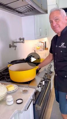 a man standing in a kitchen next to a yellow pan on the stove top and holding a spatula