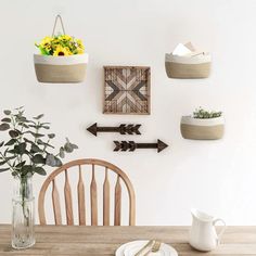 a wooden table topped with plates and bowls filled with flowers next to wall hangings