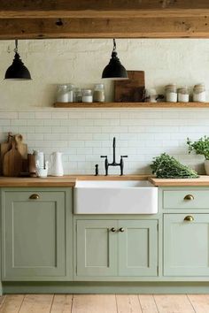 a kitchen with green cabinets and white subway tile backsplash, black pendant lights over the sink