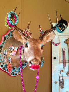 a deer head mounted to the side of a wall with beads on it's antlers