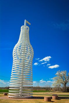 a tall white sculpture sitting on top of a lush green field under a blue sky