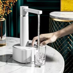 a person is pouring water from a faucet into a glass on a marble table