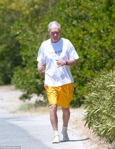 an older man in yellow shorts is walking down the road