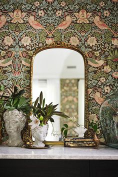 a mirror sitting on top of a table next to vases filled with flowers and plants