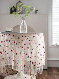 a vase with flowers on top of a table next to a window and a chair