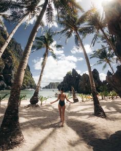 a woman in a bathing suit walking on the beach with palm trees and water behind her