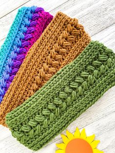 four crocheted headbands on top of a wooden table next to a sunflower