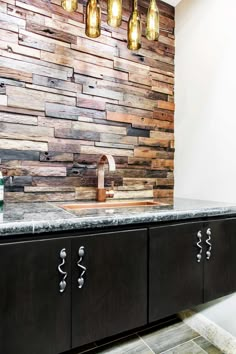 a kitchen with black cabinets and marble counter tops, hanging lights above the sink in front of a wood paneled wall