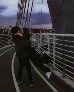 a man and woman kissing while standing on the side of a bridge in black and white