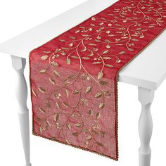 a red table runner with gold leaf designs on the edge and a white wooden table