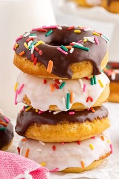 three donuts with frosting and sprinkles are stacked on a plate