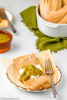 a white plate topped with fish covered in green sauce next to two bowls filled with food