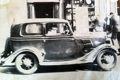 an old black and white photo of a car in front of a gas station with two men