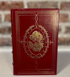 a red and gold book sitting on top of a white table next to a brick wall