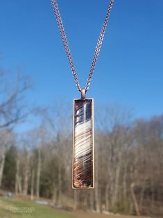 a pendant is hanging from a chain in front of some trees and blue sky with no clouds