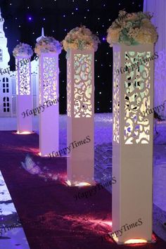 an outdoor event with tall white pillars and flowers on the floor, lit up at night