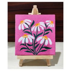 a small easel holding a pink and white flower painting on it's side