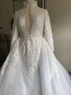 a white wedding dress with long sleeves and sheer tulle on display in a room