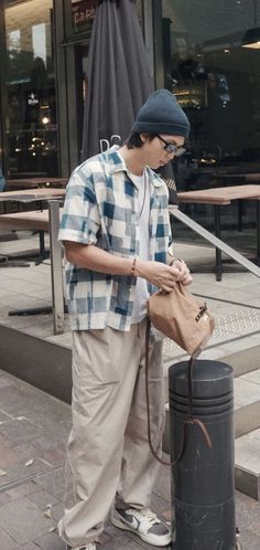 a man standing next to a trash can on the side of a street while looking at his cell phone