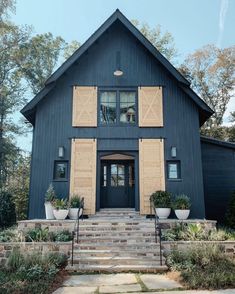 a black house with two large windows and steps leading up to the front door is surrounded by greenery