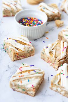 several pieces of cake with white frosting and sprinkles next to a bowl of confetti