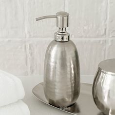 a silver soap dispenser sitting on top of a counter next to two white towels