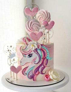 a cake decorated with pink and white icing has a unicorn on it, surrounded by heart shaped lollipops