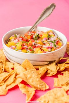 a white bowl filled with salsa surrounded by tortilla chips on a pink surface