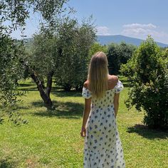 a woman in a white dress walking through an apple orchard with her back to the camera