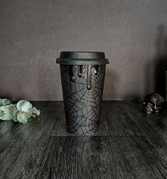 a black vase sitting on top of a wooden table next to a skull and plant