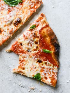 two slices of pizza sitting on top of a white counter next to each other with basil and mozzarella toppings