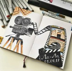 an open book with a drawing of a movie camera on it and pencils next to it